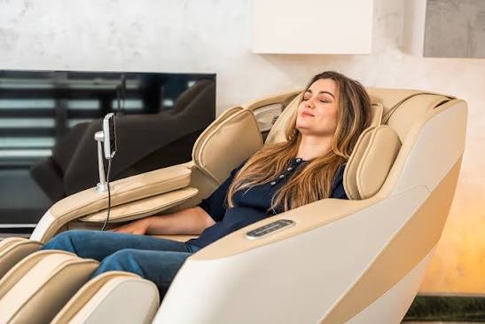 Woman relaxing in a cream full-body massage chair with a tablet controller beside her